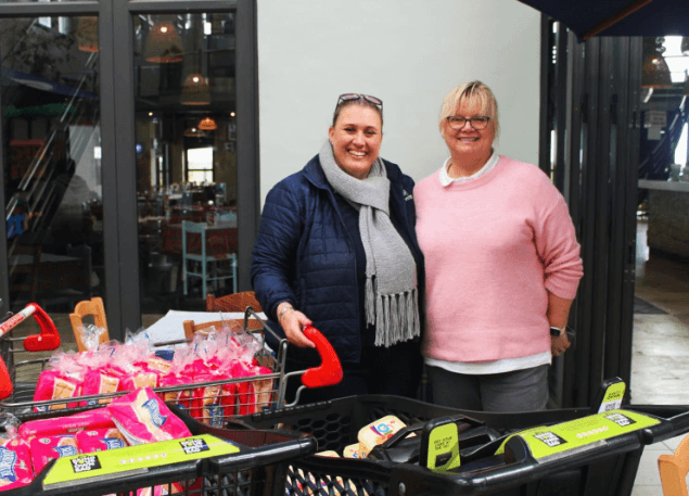 Two volunteers posing with food trolleys and donation packs.